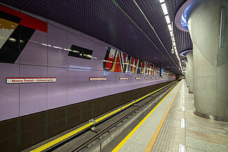 Metro station in Warsaw with ceramic tiles in the waiting area and a purple wall with colourful lettering next to the tracks.