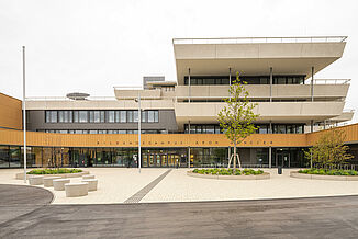 Front view of the Aaron Mencer Campus in Vienna with a façade made of wood, concrete and glass and surrounding terraces on several floors.