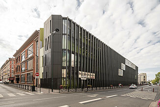 Corner view of the modern building with a dark façade and many windows, which houses the Léo Délibes music school in Paris.