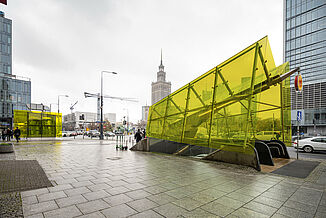Metro entrance with yellow glass roof between residential and commercial buildings in Warsaw.