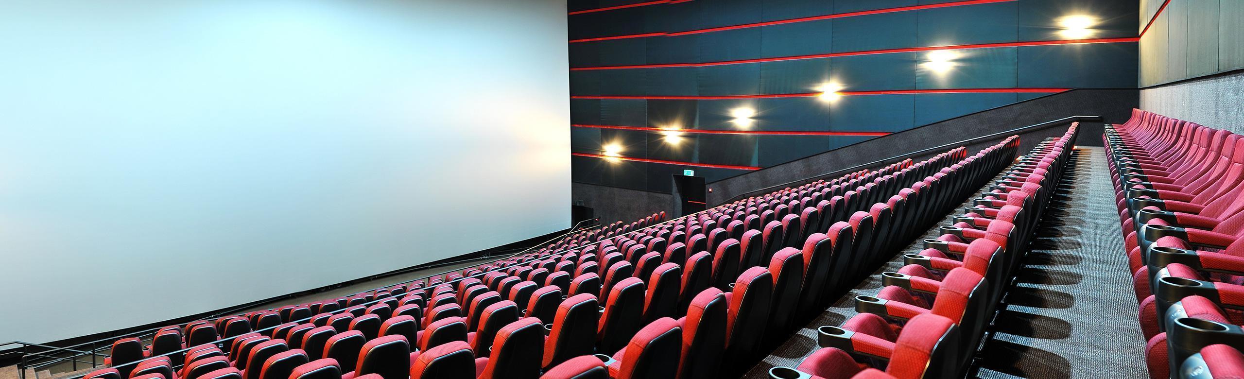 A large cinema hall with red armchairs and a big screen.