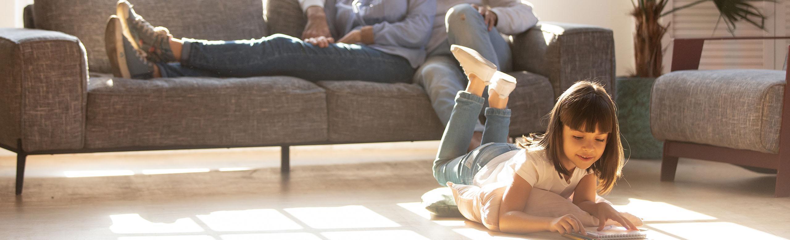 A girl is lying on the living room floor reading a book.